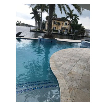 A freeform pool with a raised spa and travertine deck on a canal waterfront.