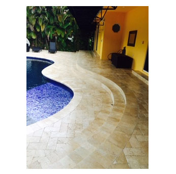 A curving travertine paver deck wraps around the edge of a freeform pool under a covered lanai.