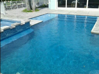 A rectangular backyard pool with a tiled tanning ledge and paver deck under open sky.