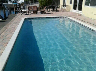 A small rectangular pool with a paved deck next to a canal with boats.