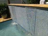 Close-up of a mosaic tile wall with water spilling into a pool corner.
