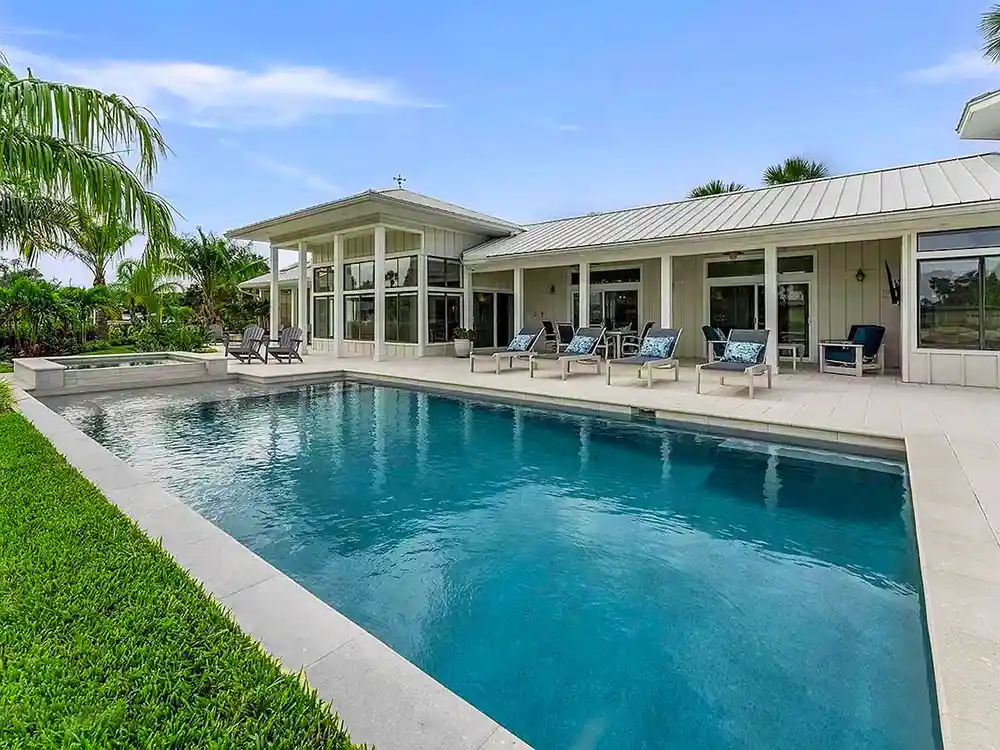 A rectangular backyard pool with a raised spa alongside a modern ranch-style home under open sky.