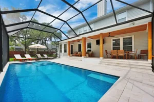 A rectangular pool with a tanning ledge under a screened lanai next to a two-story home with a covered porch.