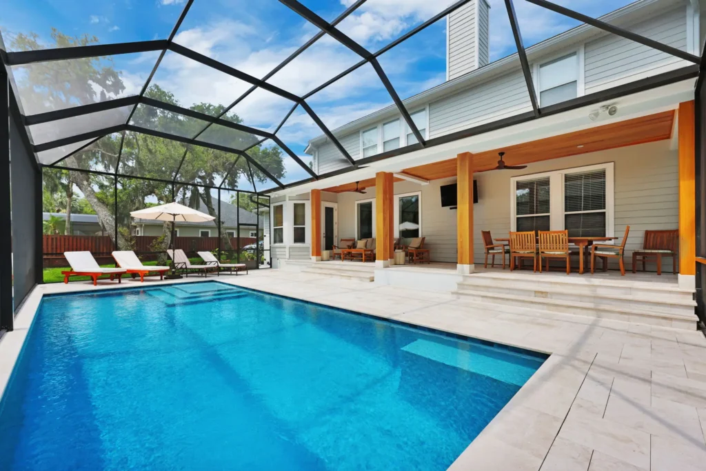 A rectangular pool with a tanning ledge under a screened lanai next to a two-story home with a covered porch.