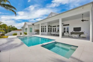A rectangular backyard pool with a separate square spa in front of a white covered outdoor living pavilion.