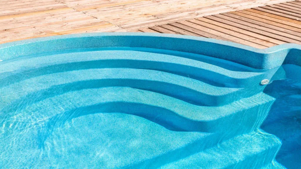 Close-up of curved molded fiberglass pool steps beside a wooden deck.