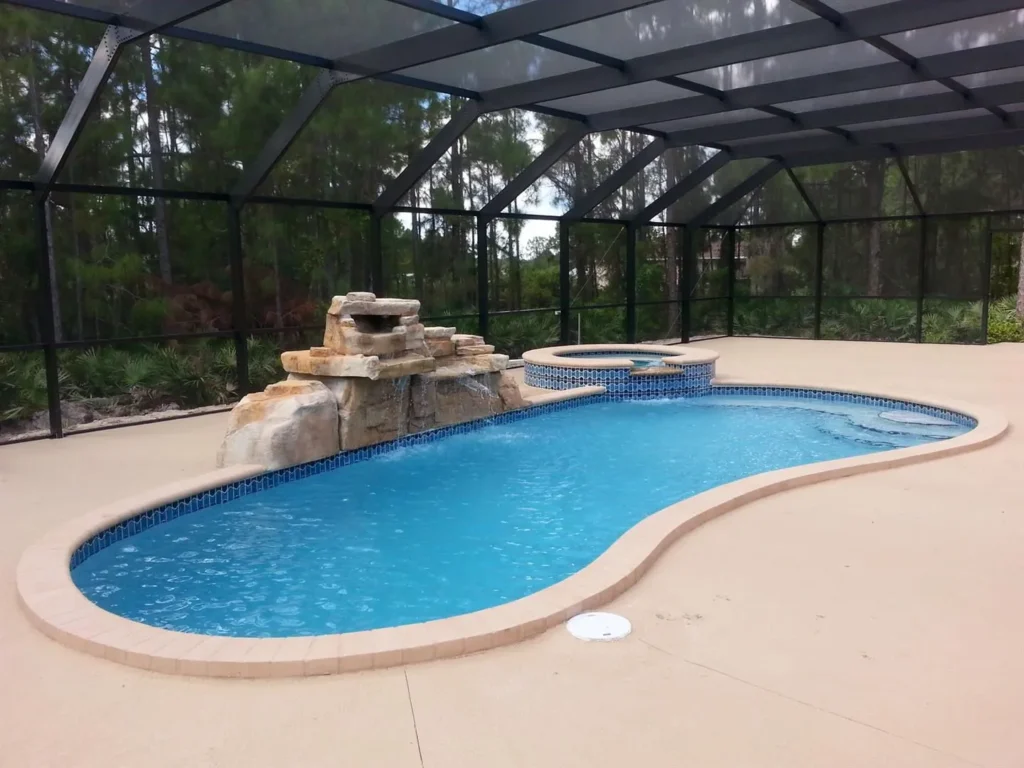 A kidney-shaped pool with a raised spa and rock waterfall feature inside a screened enclosure surrounded by trees.