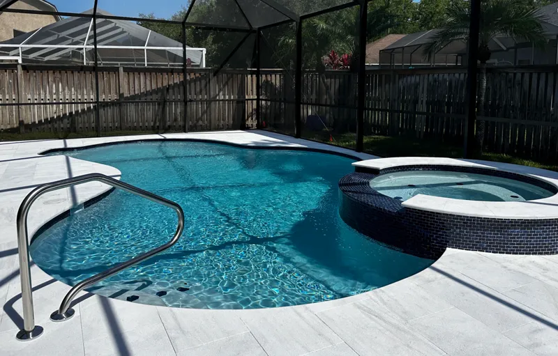 A freeform pool with a raised spa under a screened enclosure in a suburban backyard.