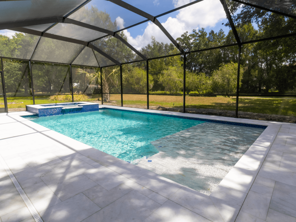 A rectangular pool with a raised tiled spa sits under a screened enclosure with a shallow baja shelf entry.