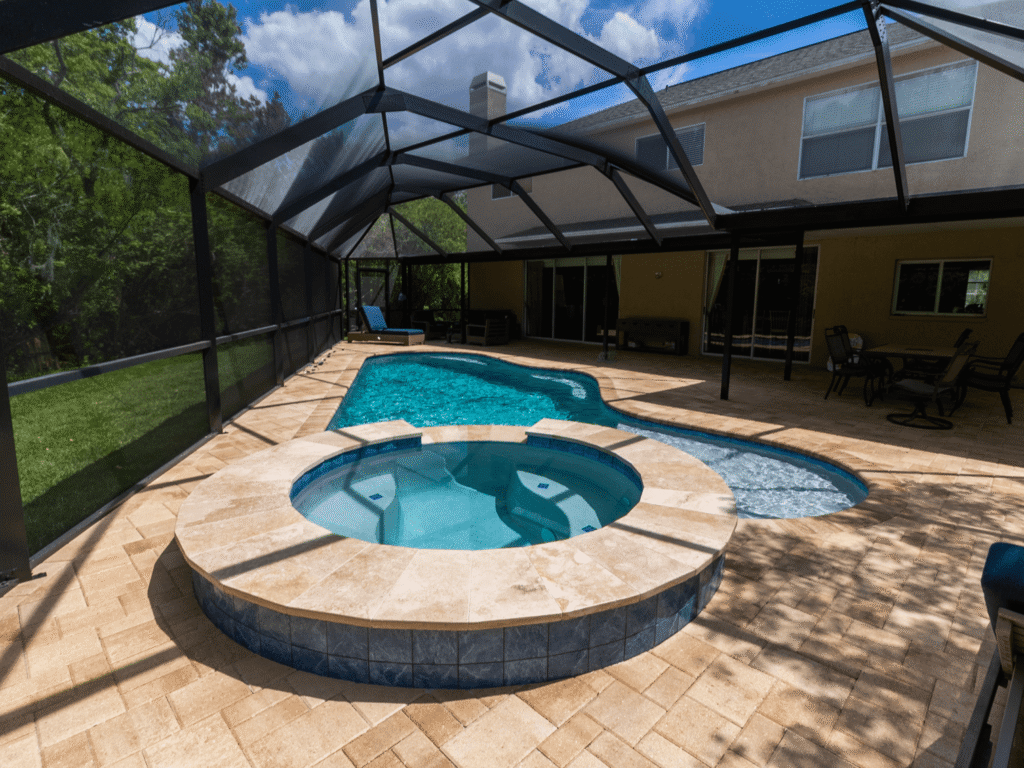 A raised round spa with a stone-clad wall spills over into a freeform pool under a screened patio enclosure.
