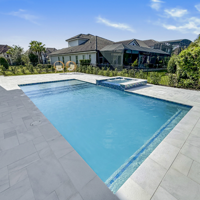 A rectangular pool with a raised spa in the corner of a paved backyard patio.