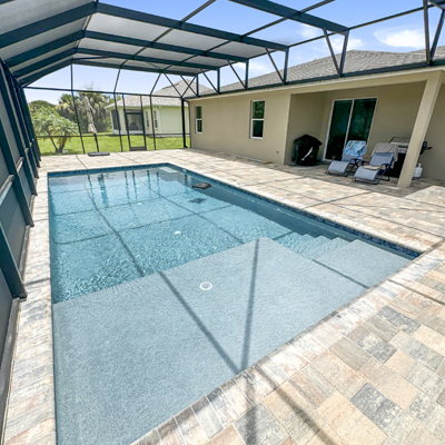 A rectangular pool with a shallow entry ledge under a screened patio enclosure.