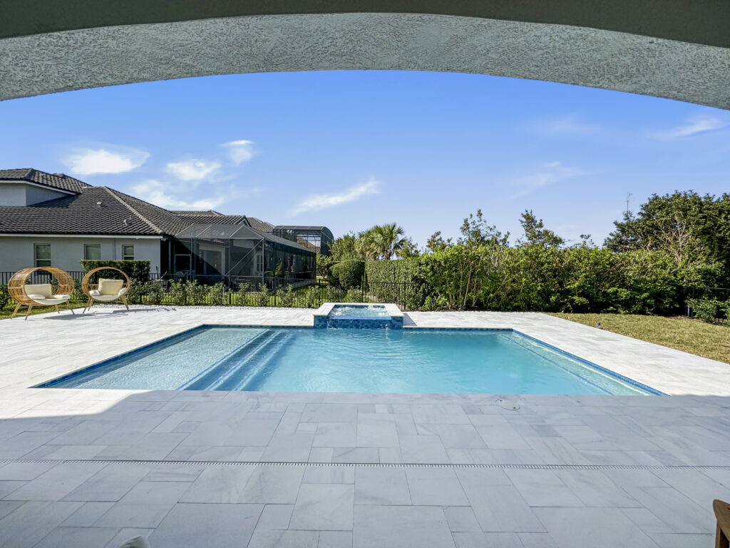Rectangular backyard pool with a raised spillover spa, viewed through a stone arch under a covered patio.