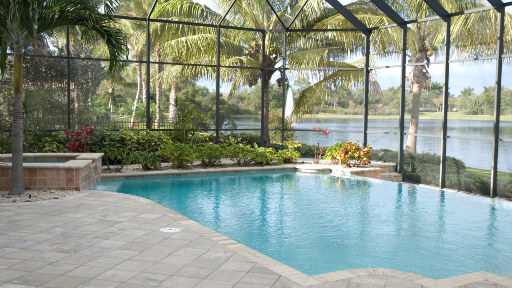 Freeform pool with raised spa under a screened lanai overlooking a lake with palm trees.