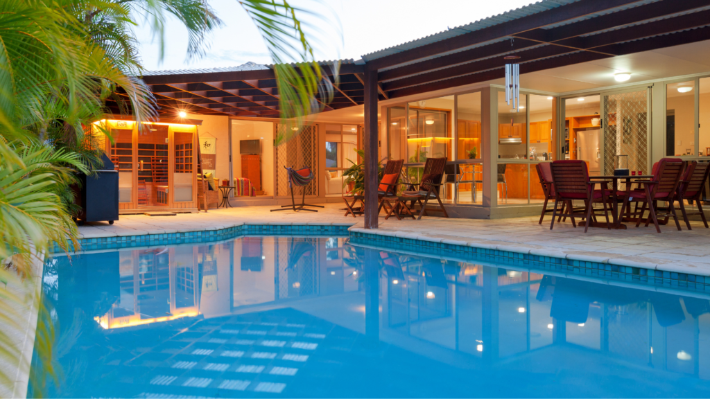 A pool at dusk with reflections of a covered patio and house alongside it, outline not fully traceable.