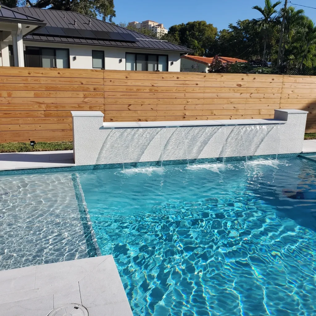 A raised stone wall with a row of sheer waterfall jets cascading into the corner of a pool.
