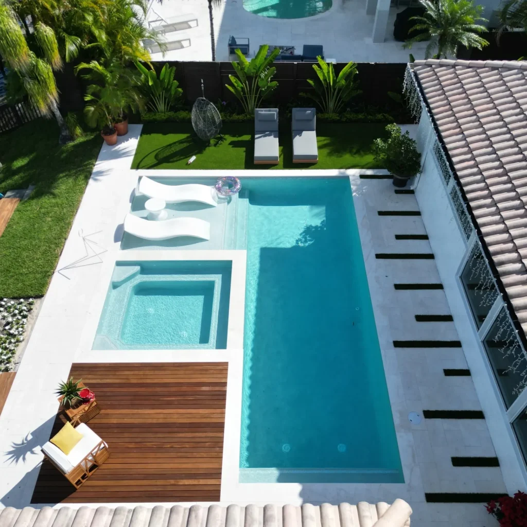 Aerial view of a modern rectangular pool with an attached spa, wood sundeck, and lush landscaped backyard.