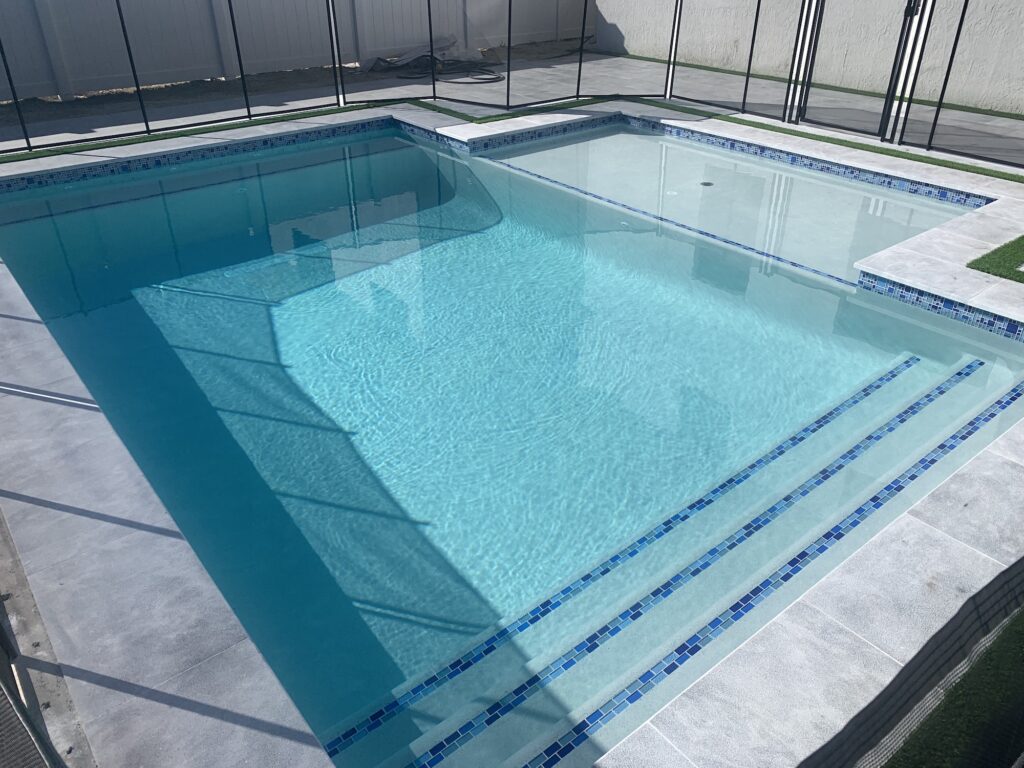 A rectangular backyard pool with a raised-looking but flush spa, tiled steps, and a paver deck enclosed by a removable safety fence.
