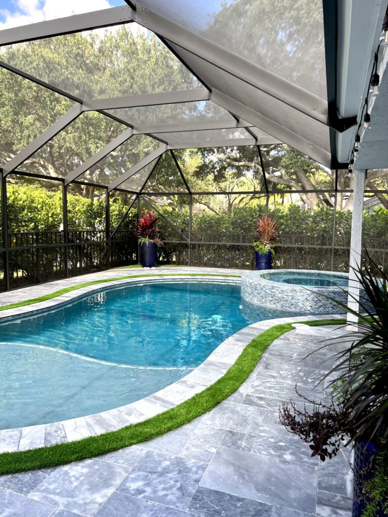 Freeform pool with raised tiled spa under a screened lanai with travertine deck and turf edging.