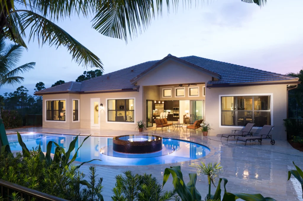A dusk view of a freeform pool with a raised round spa in front of a single-story Florida home.