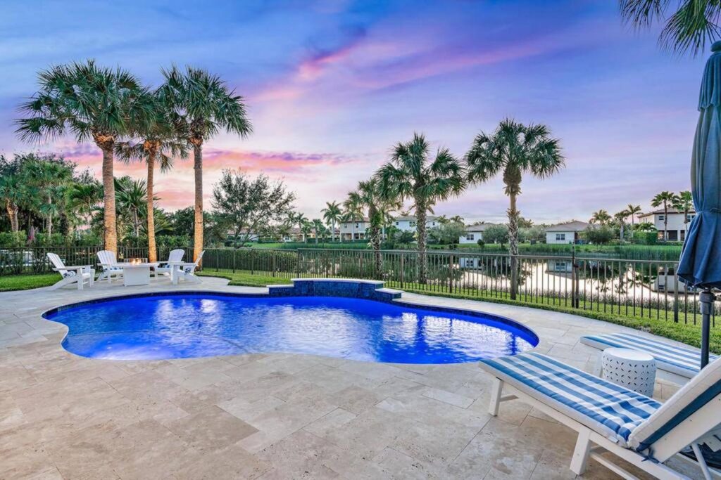 A freeform pool with raised spa on a travertine patio overlooking a lake at dusk.