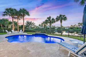 A freeform pool with raised spa on a travertine patio overlooking a lake at dusk.
