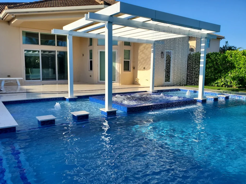 A raised tiled spa with a pergola and rain-curtain water feature sits in the center of a geometric pool with stepping pads leading across it.