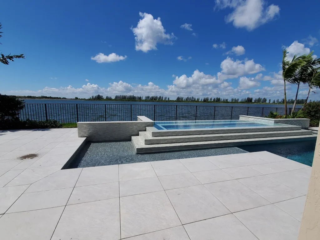 An elevated tiled spa spills over steps into a pool with a canal view in the background.