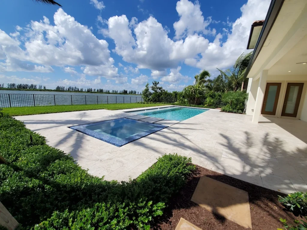 A rectangular pool with an attached raised spa on a travertine patio overlooking a lake.