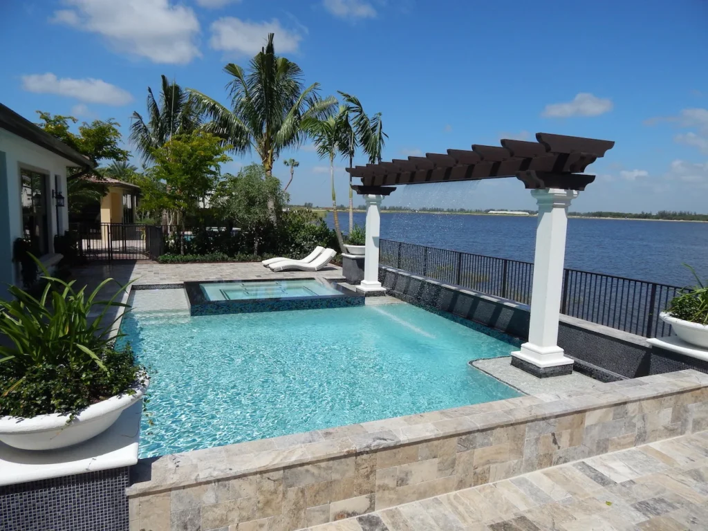 An infinity-edge style rectangular pool with a raised spa and waterfall pergola overlooking a wide waterway.
