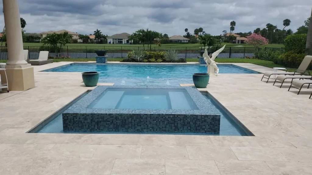 A raised mosaic-tiled spa sits in the foreground with a rectangular pool and lake view behind it.