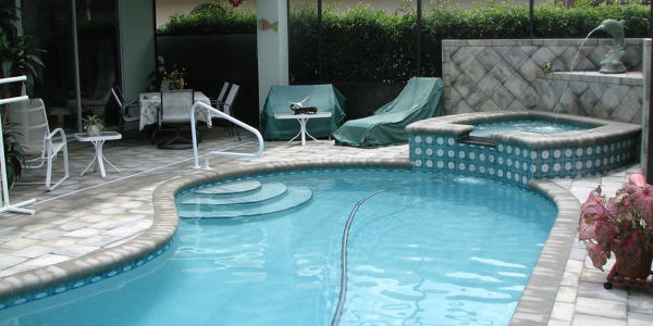 A freeform backyard pool with steps and an adjacent raised spa under a screened patio enclosure.
