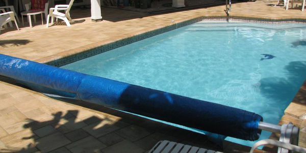 A small rectangular backyard pool with a blue solar cover partially rolled onto a reel.