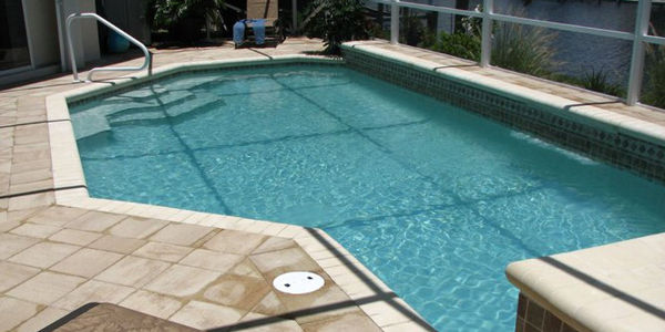A rectangular pool with cut-corner steps under a screened enclosure beside a canal.