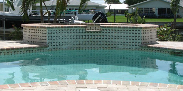 A raised spa with decorative mosaic tile sits beside a pool on a canal-front property.