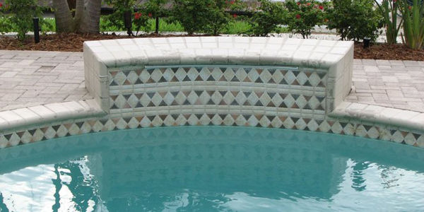 Close-up of a pool's raised wall edge decorated with a diamond mosaic tile band.