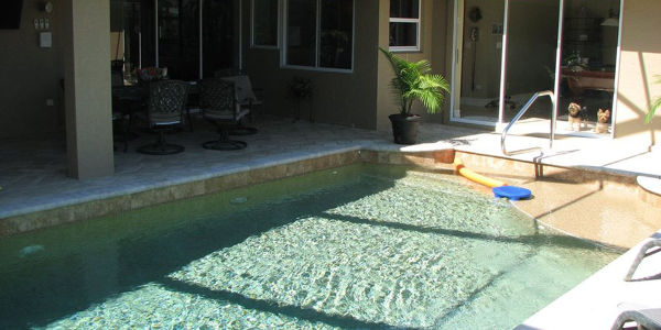 Small rectangular backyard pool with a shallow entry step and covered patio seating area.