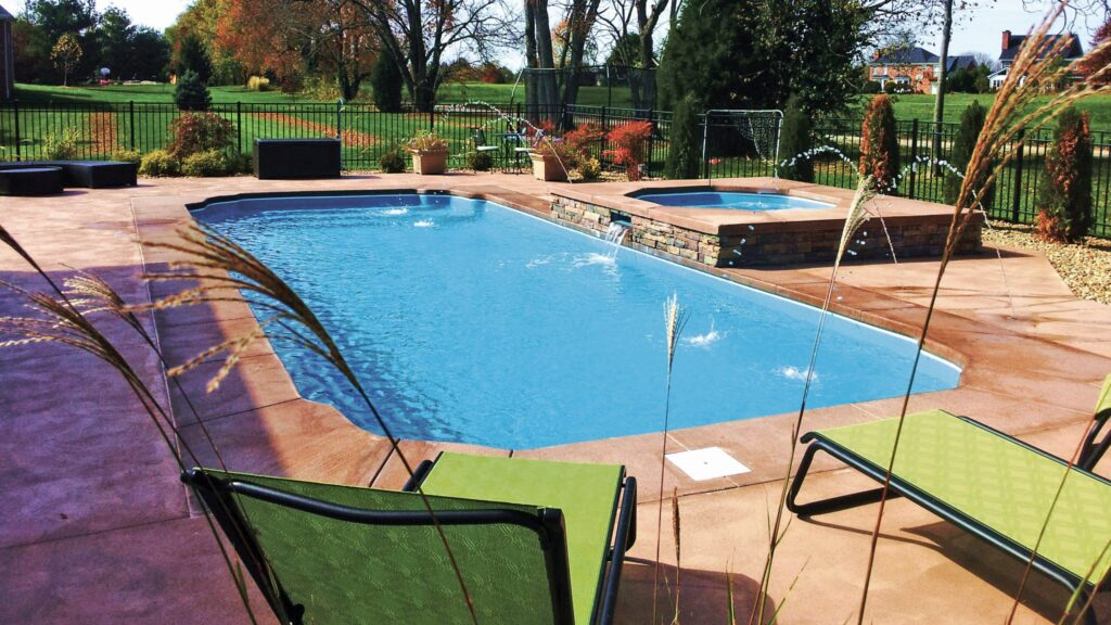 An L-shaped fiberglass pool with a raised spa and stone waterfall on a stamped concrete patio.