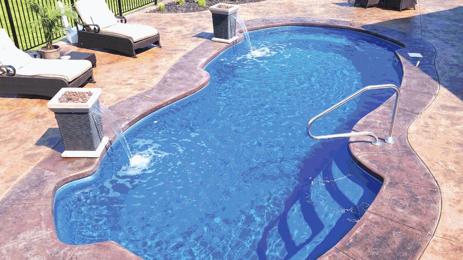 A freeform fiberglass pool with two pedestal water fountains on a stamped concrete patio with lounge chairs.