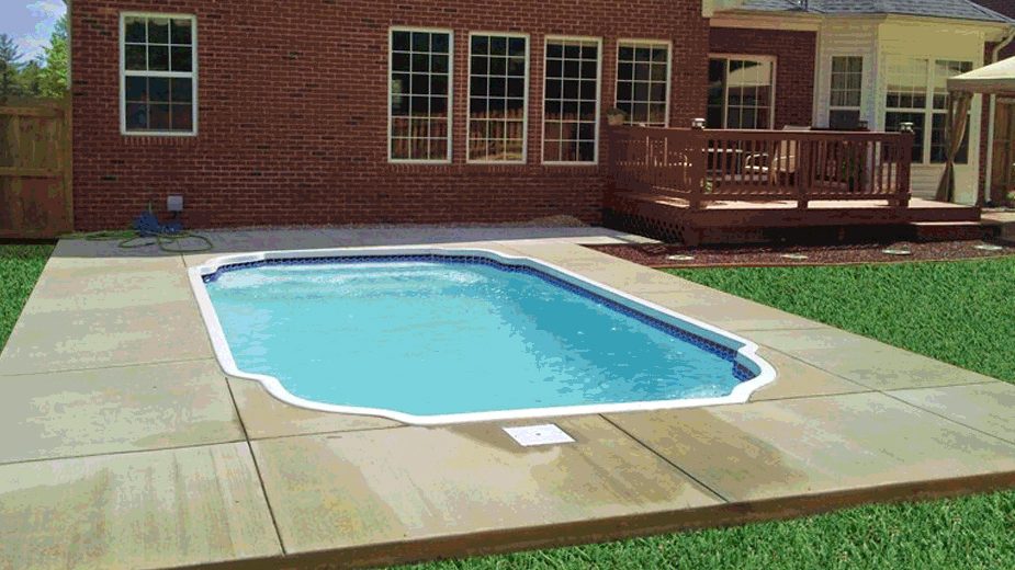 A small octagonal fiberglass pool with blue tile trim set in a concrete patio behind a brick house.
