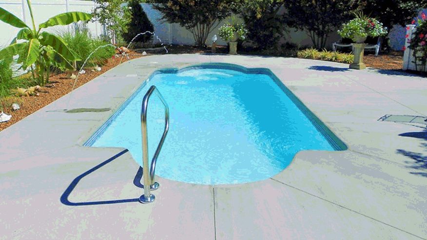 A small rectangular fiberglass pool with rounded end and steel handrail on a concrete patio.