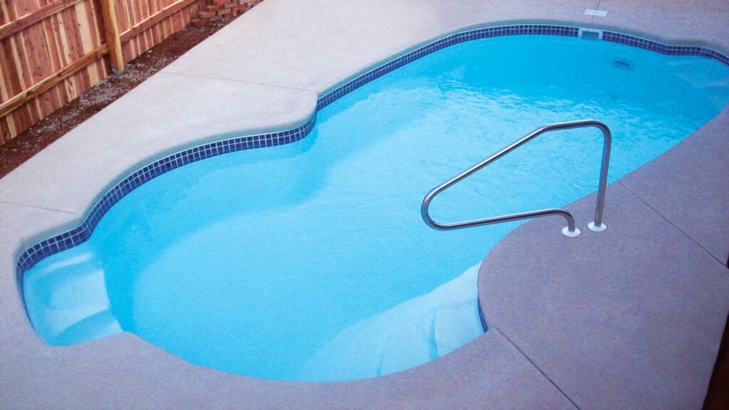 An overhead view of a small kidney-shaped fiberglass pool with blue tile trim and a stainless handrail.
