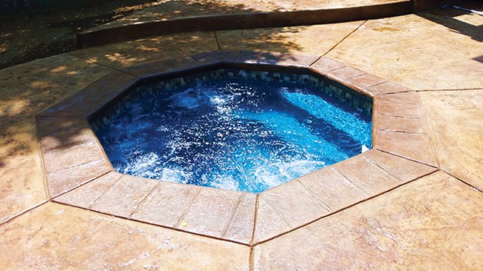 An octagonal spa with bubbling jets set into a stamped concrete patio.