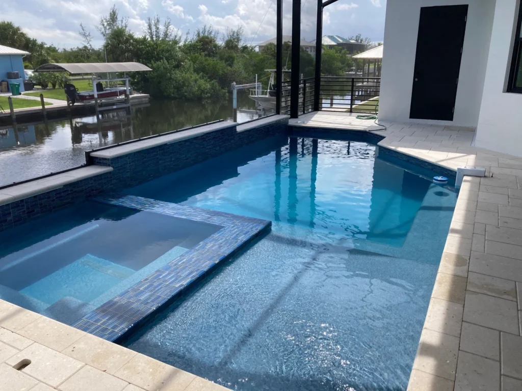 A rectangular pool with an integrated raised spa and canal view under a screen enclosure.