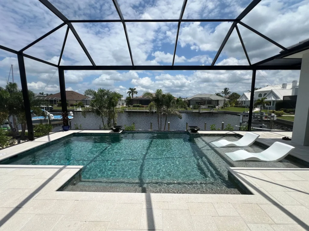 A modern rectangular pool with a sun shelf and two loungers under a screened enclosure overlooking a canal.