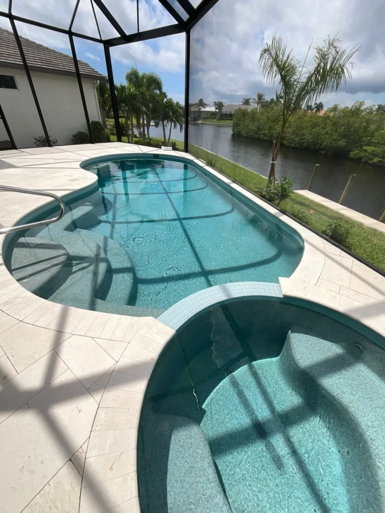 A freeform pool with an attached spa under a screened lanai overlooking a canal.