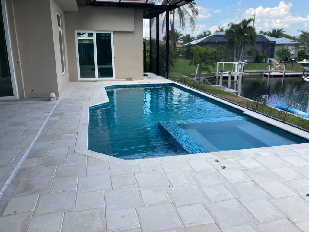 A modern rectangular pool with a raised sun shelf and integrated spa beside a screened lanai overlooking a canal.