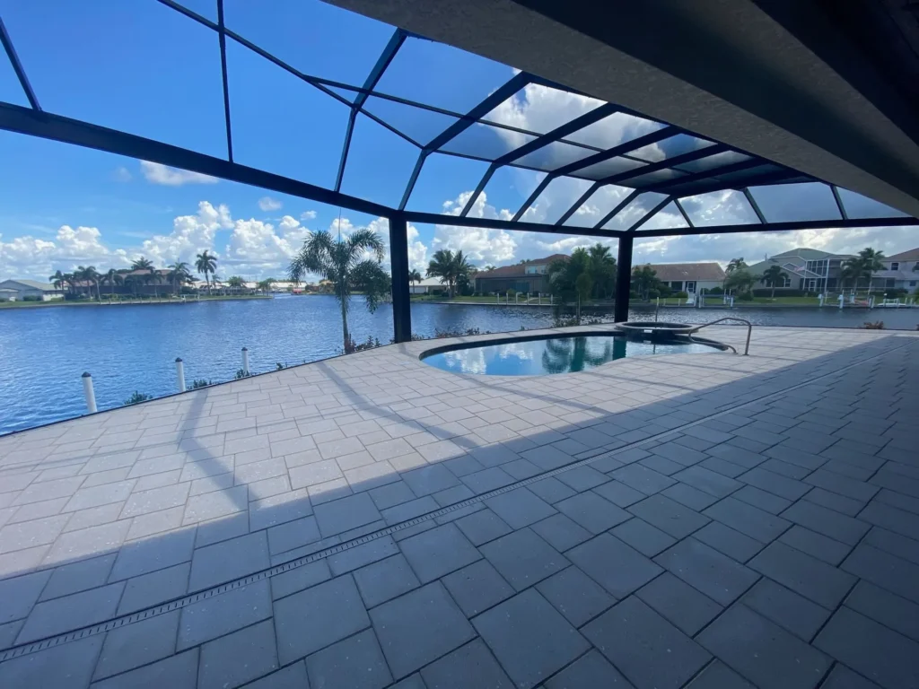 A small freeform pool under a screened enclosure overlooking a canal with palm trees and homes across the water.