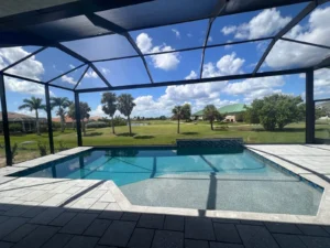 A geometric pool with a raised tiled wall sits under a screened enclosure overlooking a golf course.