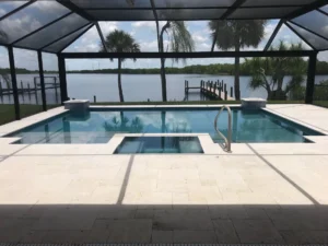 A rectangular pool with a notch cutout under a screened lanai overlooking a canal with a dock.